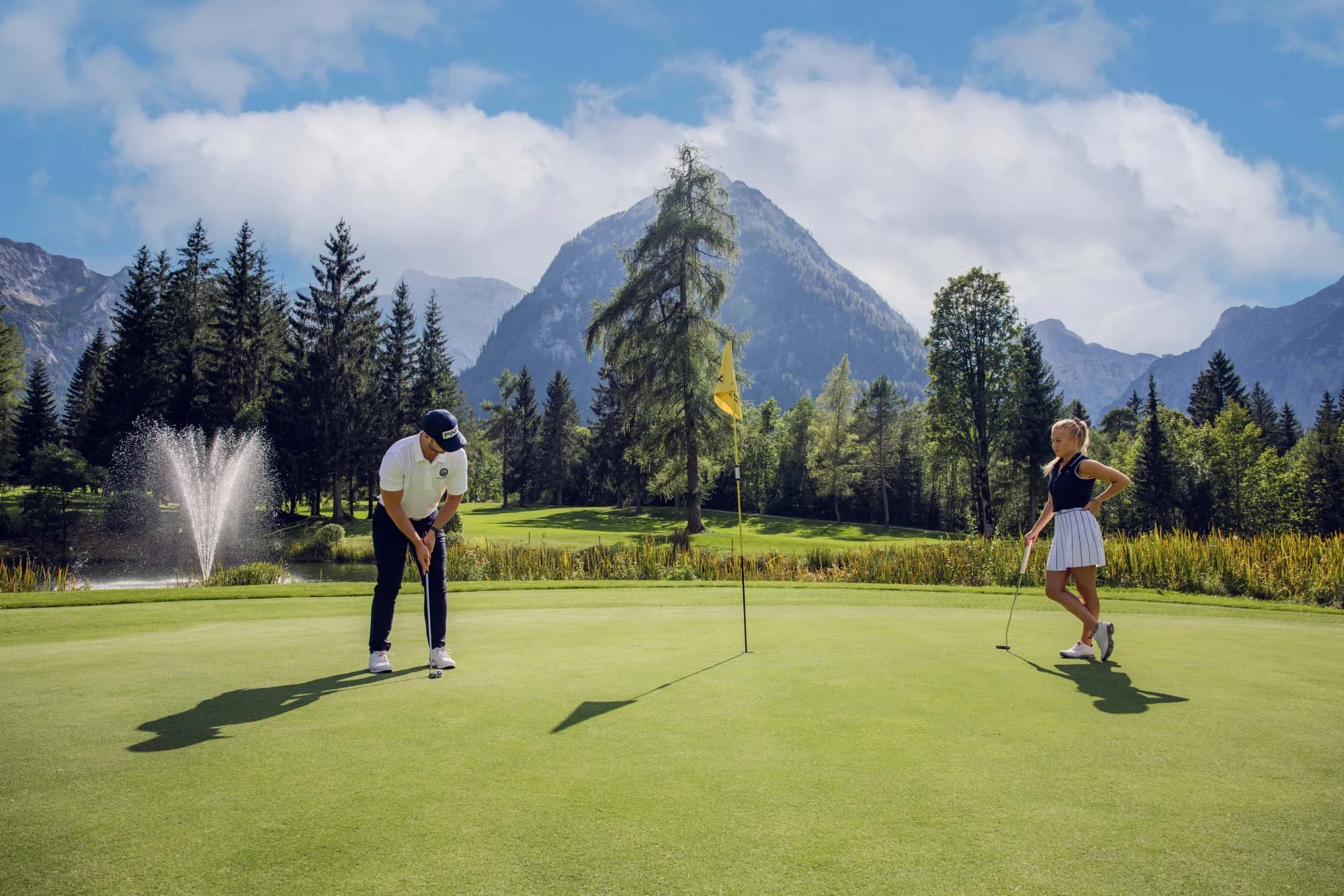 Golfpaar puttet auf dem Grün, im Hintergrund ein Springbrunnen und die Gipfel des Rofan