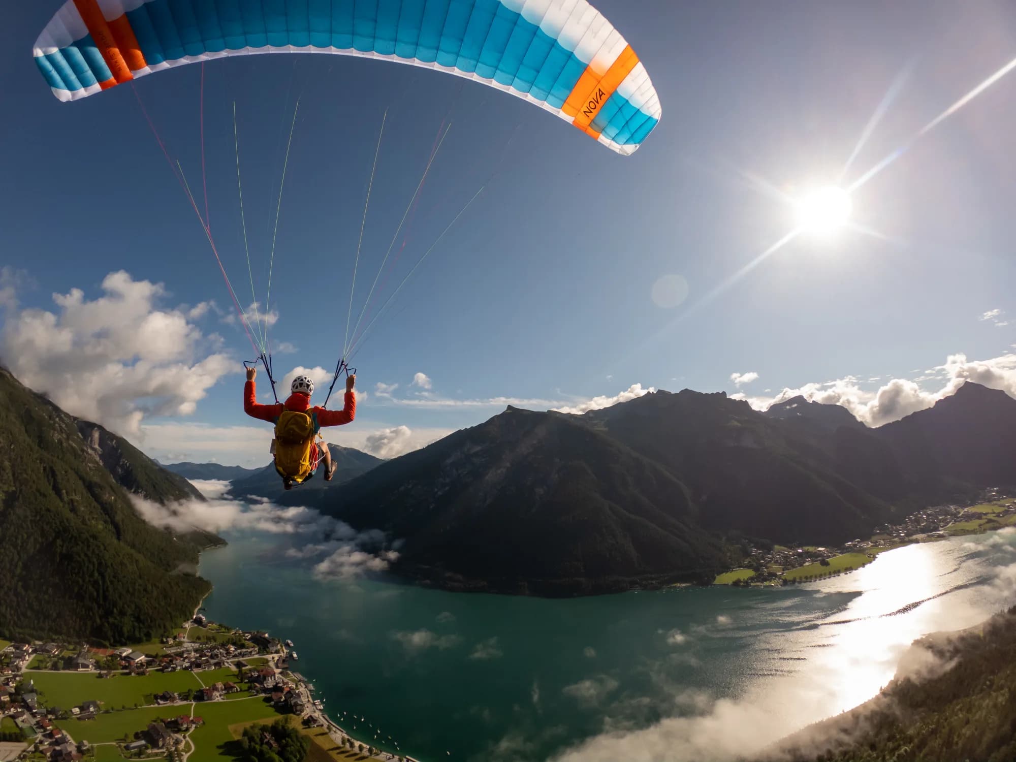 Gleitschirmpilot im Gegenlicht der Sonne hoch über dem Tal