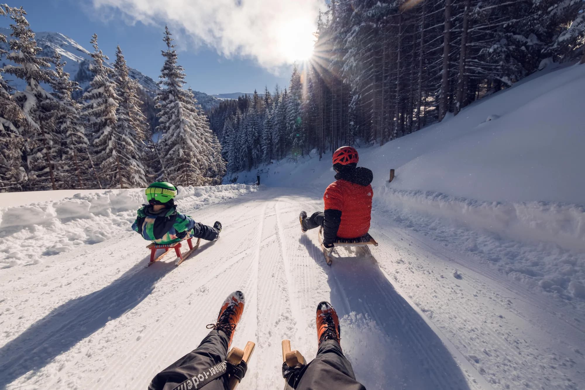 Familie rodelt hintereinander die sonnige Rodelbahn am Zwölferkopf hinunter