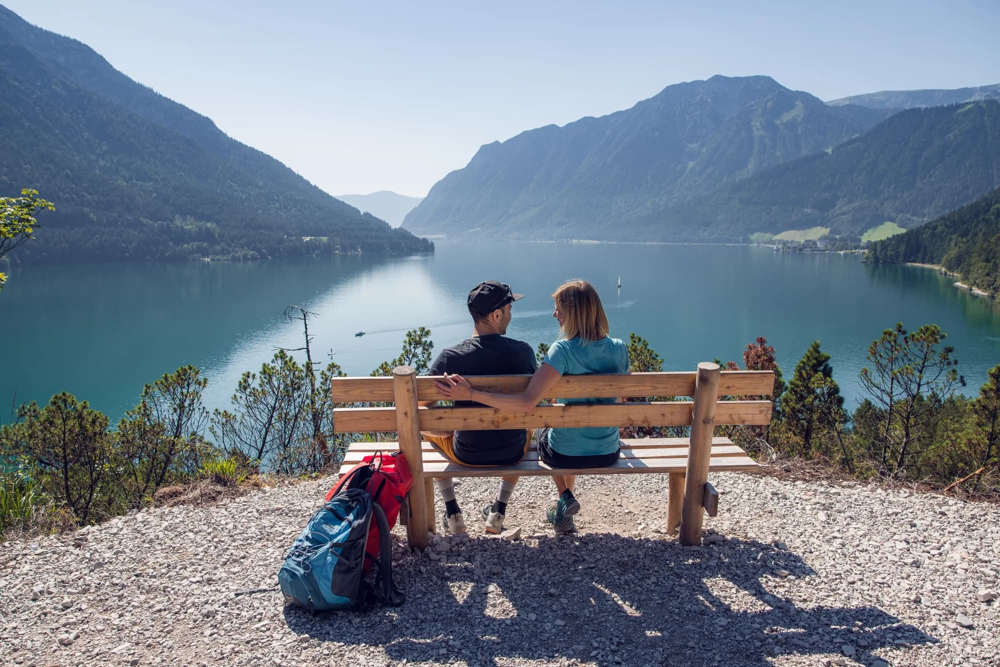 Paar rastet auf einer Holzbank am Gaisalmsteig hoch über dem türkisblauen Achensee