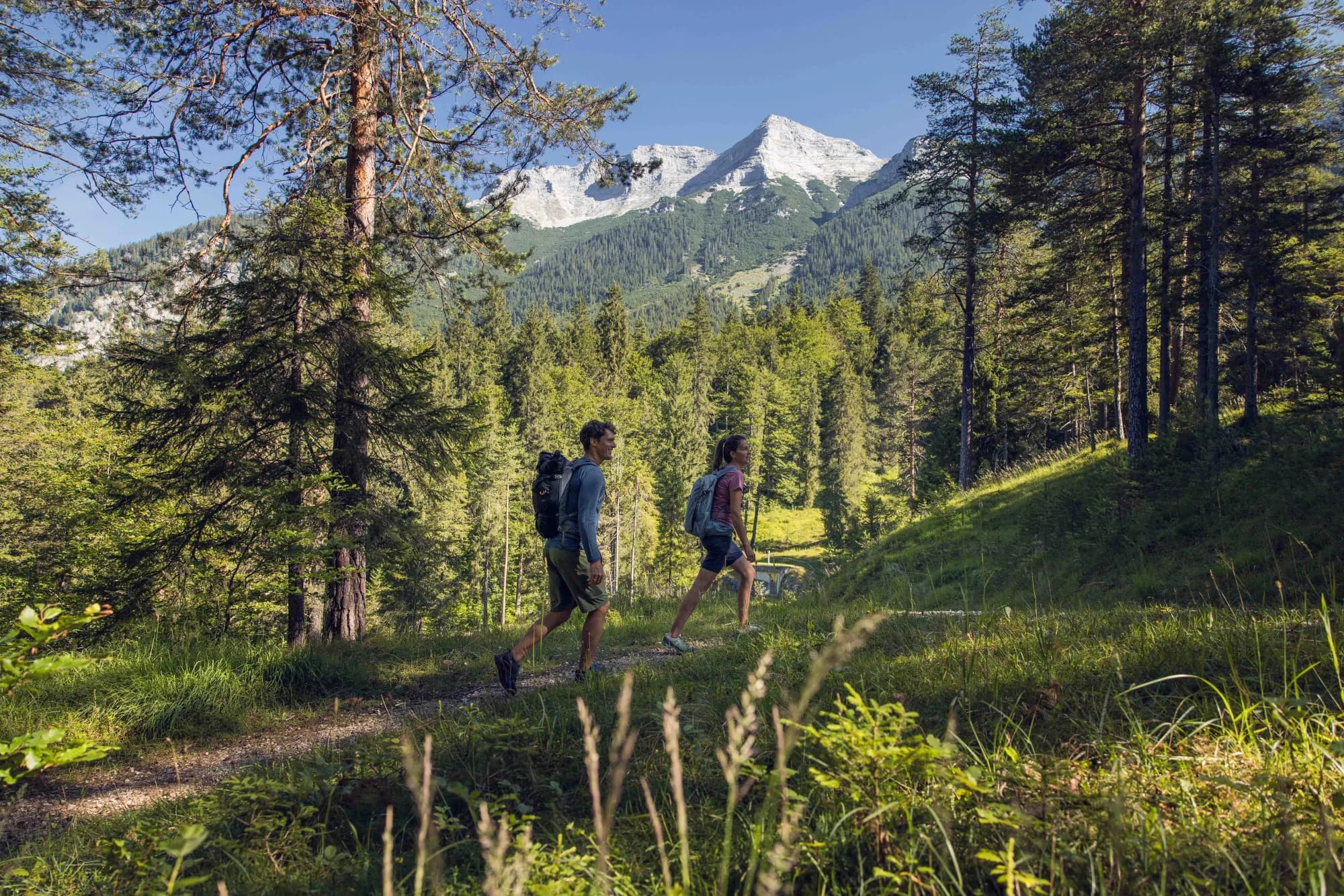 Paar wandert durch den Wald der Bärenwaldrunde in Steinberg am Rofan, im Hintergrund ein schneebedeckter Gipfel