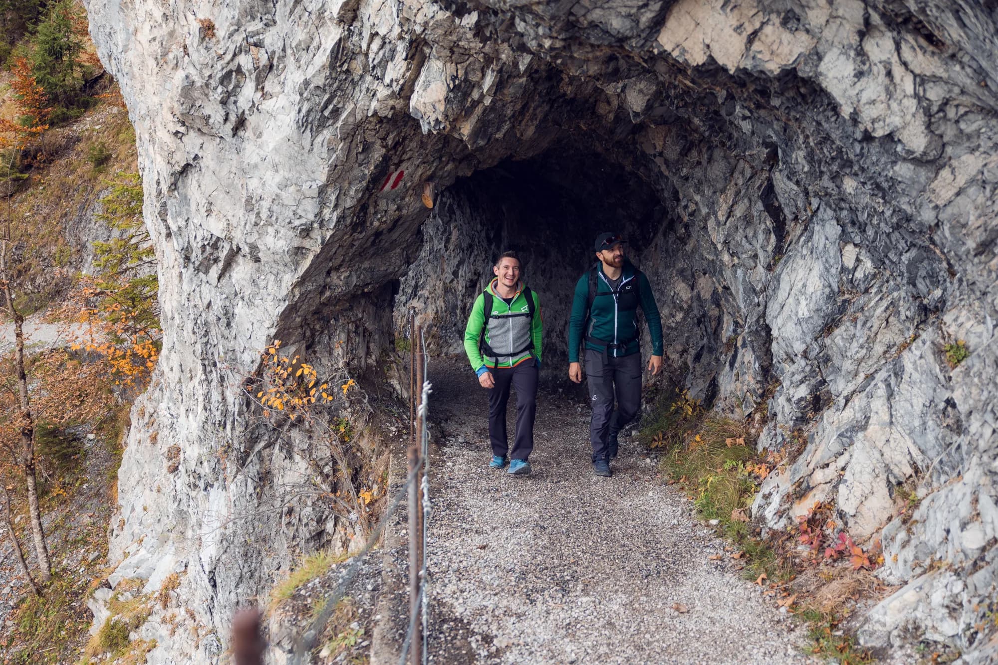 Zwei Wanderer entlang des Tunnelwegs Richtung Zwölferkopf im goldenen Herbstlicht