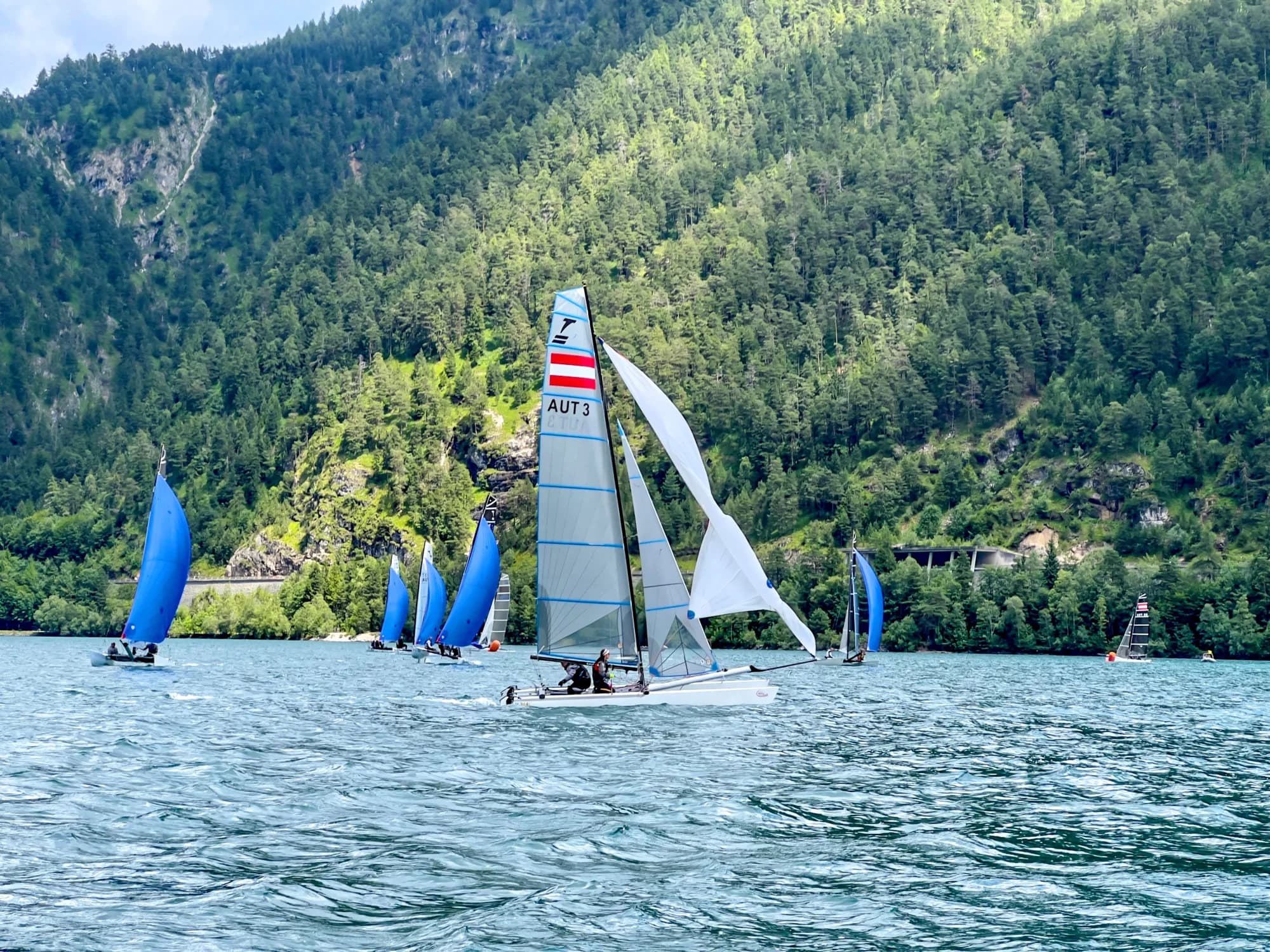 Segelboote der Tornado-Europameisterschaft am Achensee, umgeben von bewaldeten Berghängen