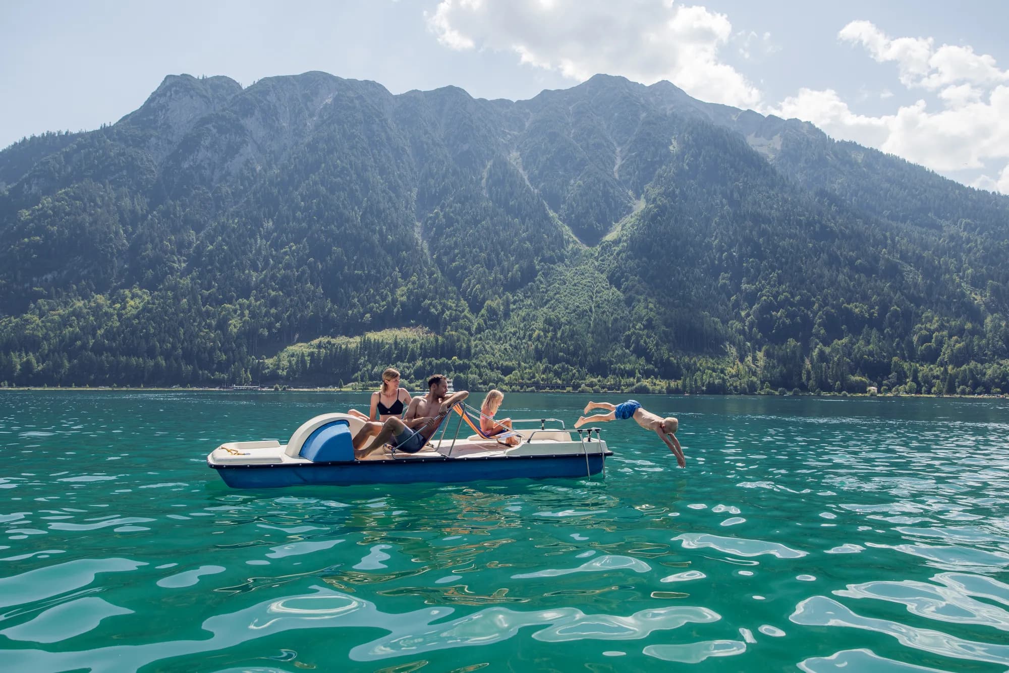 Familie im Tretboot auf dem Achensee, ein Kind springt ins türkisblaue Wasser