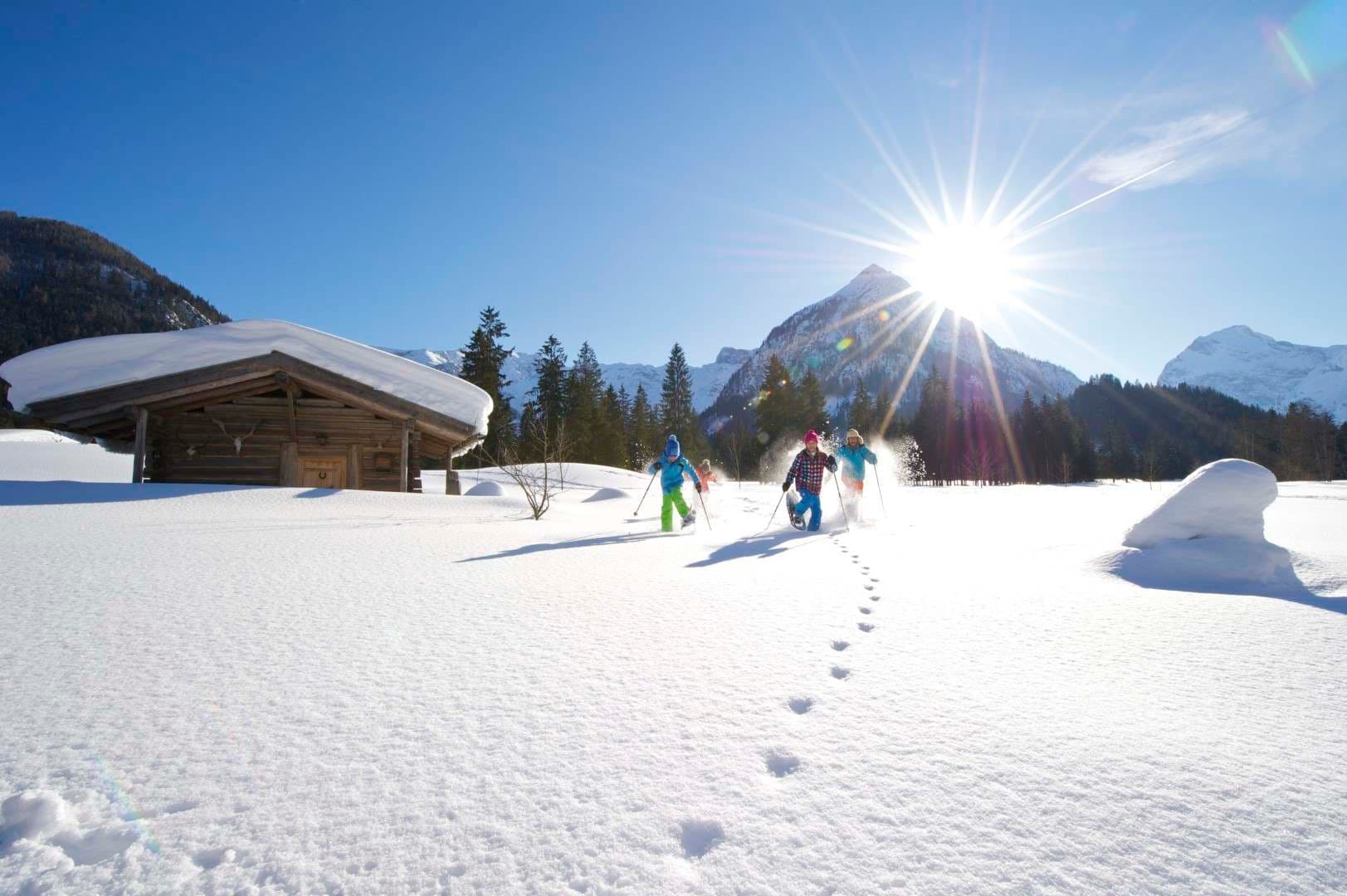 Familie beim Schneeschuhwandern vor verschneiter Hütte